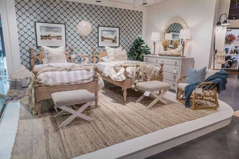 A lifestyle photo of a room with two twin size beds with wooden frames on a large tan rug with a crisscrossed accent wall